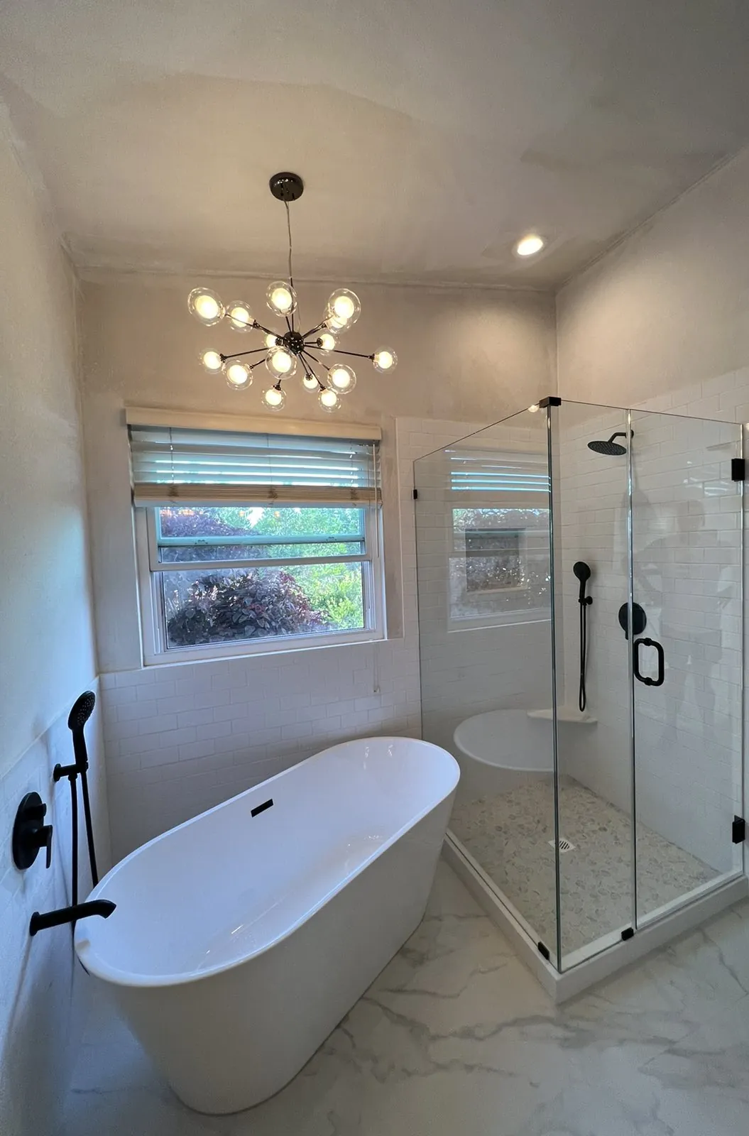 Primary bathroom with a freestanding tub, frameless glass shower, pebble shower floor and matte black fixtures