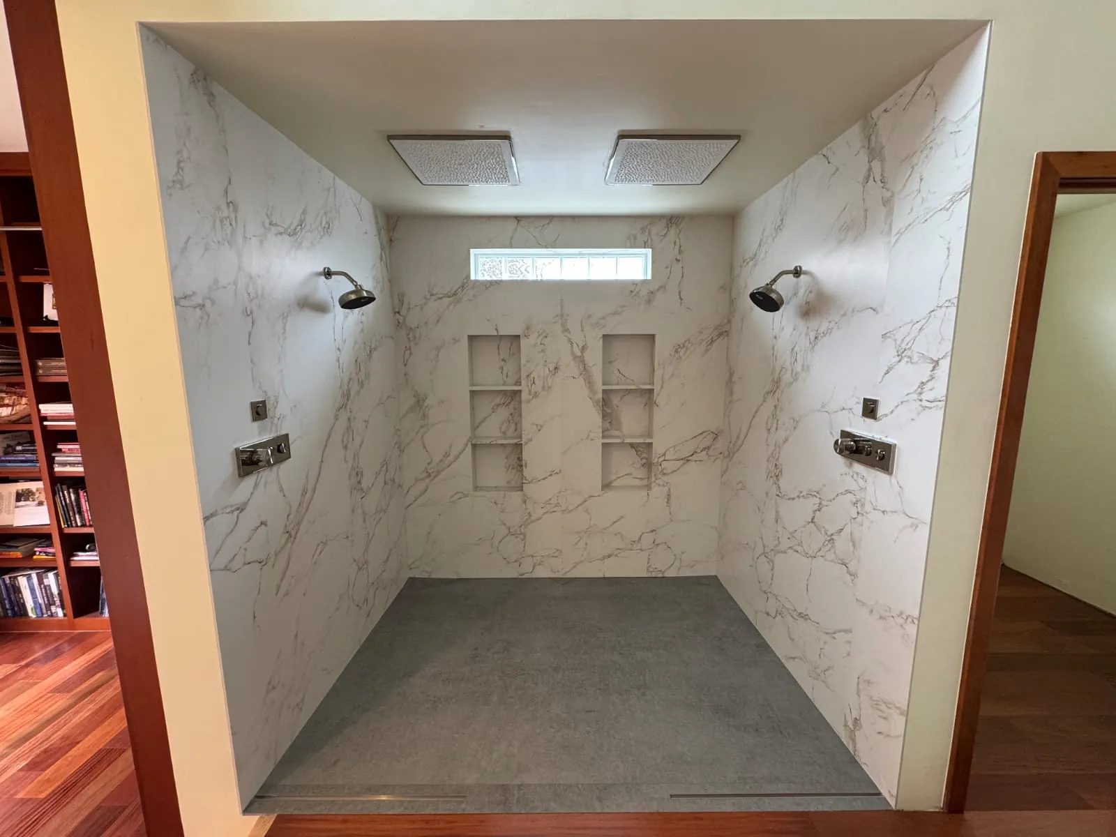 Curbless walk-in double shower with marble-look porcelain slab walls, two rain heads, recessed niches and linear drains