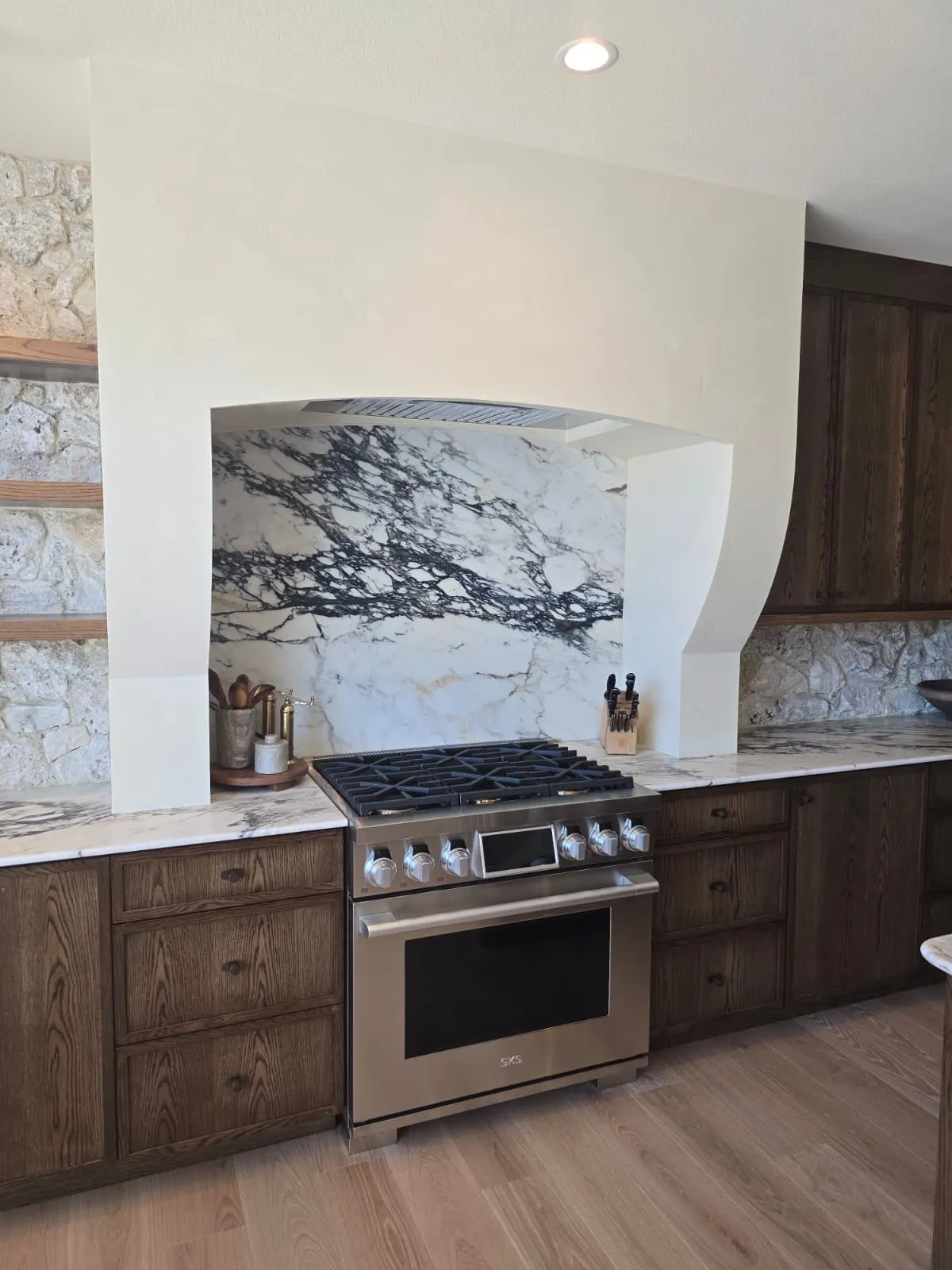 Kitchen with a custom plaster range hood, full-height marble slab backsplash and stained oak cabinetry