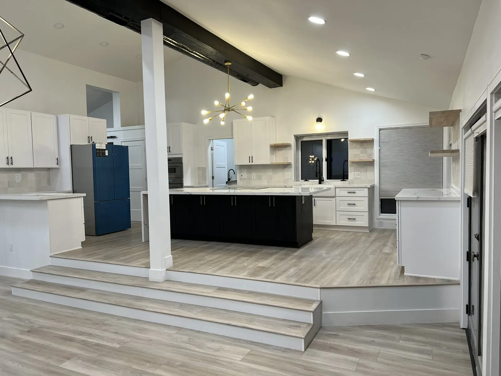 Raised kitchen platform with steps, dark island cabinetry and white shaker perimeter cabinets